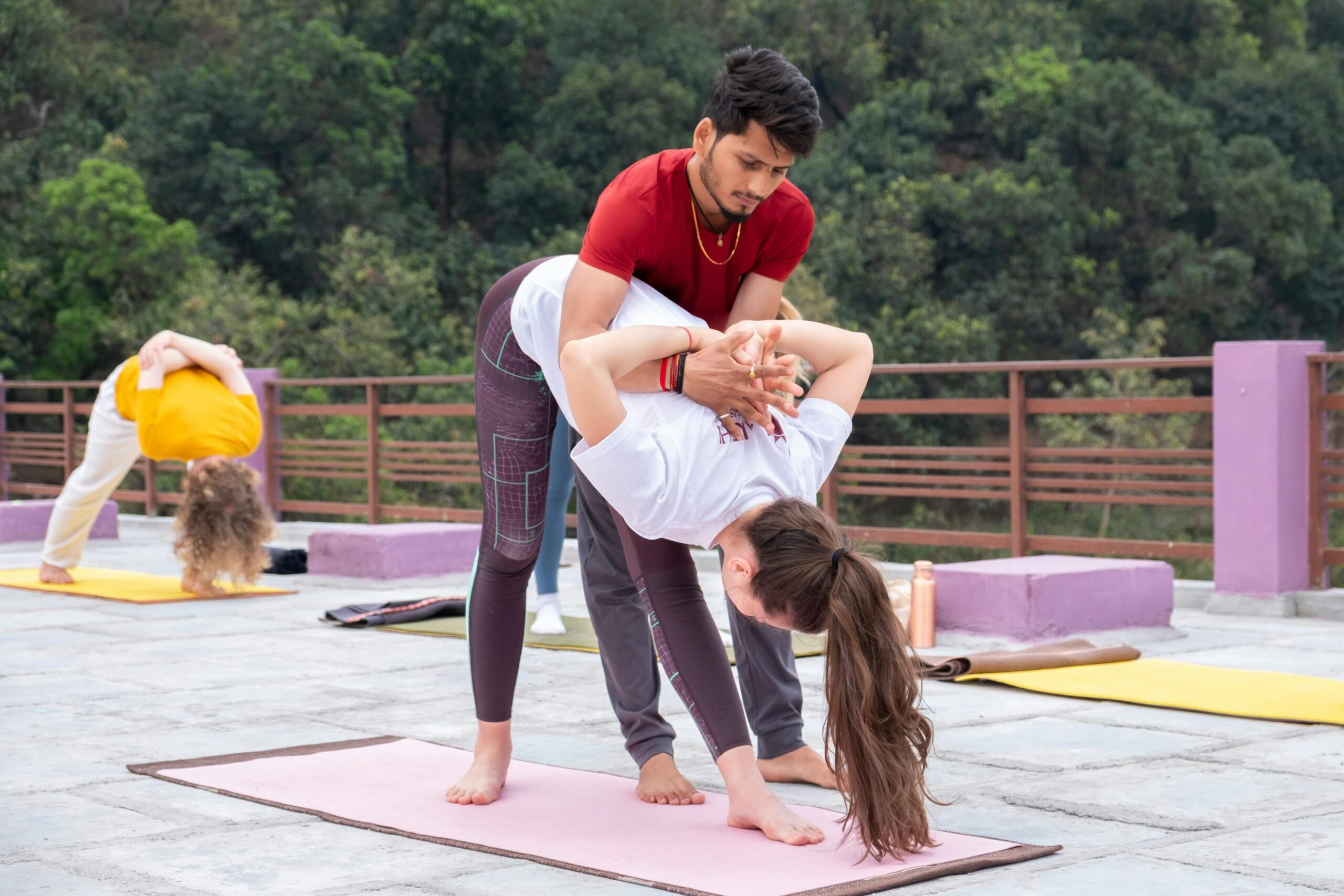 Yoga instructor helps a student with a pose outdoors. Group session amidst nature.