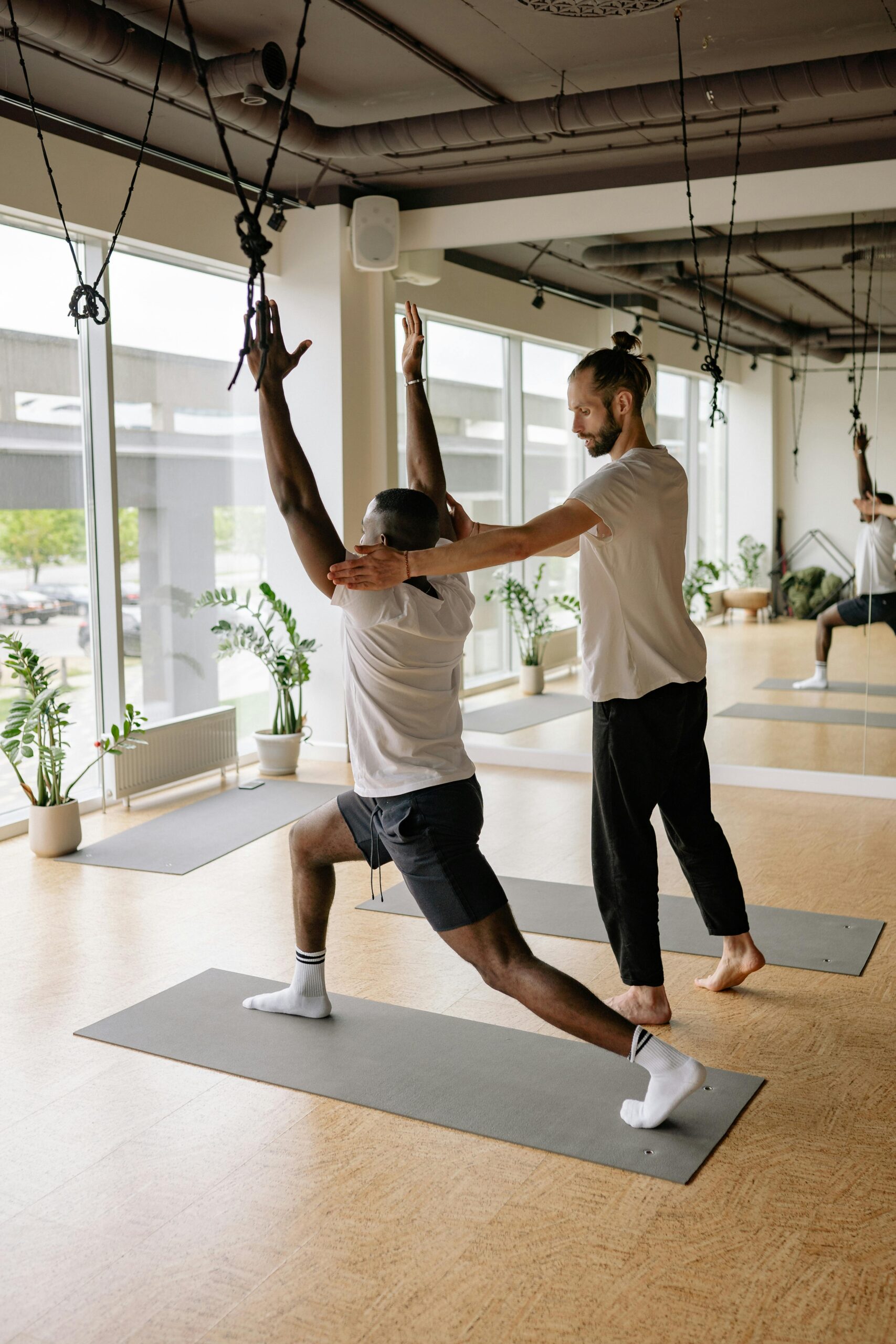 Instructor helps student with yoga pose in bright studio, promoting wellness and fitness.